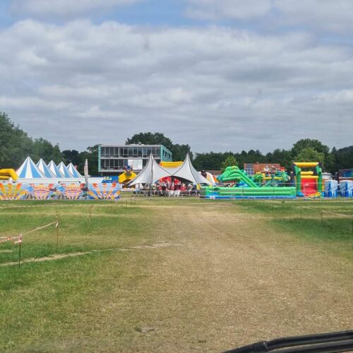 Ein bunter Jahrmarkt mit Hüpfburgen und Zelten auf einer Wiese an einem bewölkten Tag.