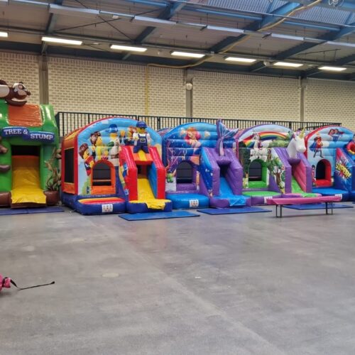 Bunte Hüpfburgen in einer Halle, mit Tiermotiven und Spielelementen, auf grauem Boden.