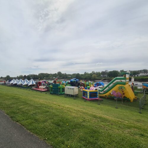 Ein weitläufiger Freizeitpark mit bunten Hüpfburgen und Zelten auf einer grünen Wiese.