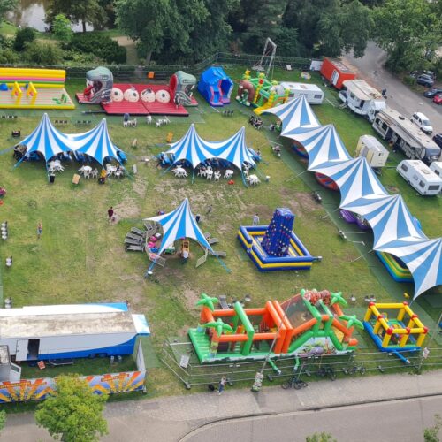 Luftaufnahme eines Spielplatzes mit bunten Hüpfburgen und blau-weißen Zelten im Grünen.